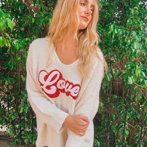 May include: A white fuzzy sweater with a red and pink "Love" graphic on the front.