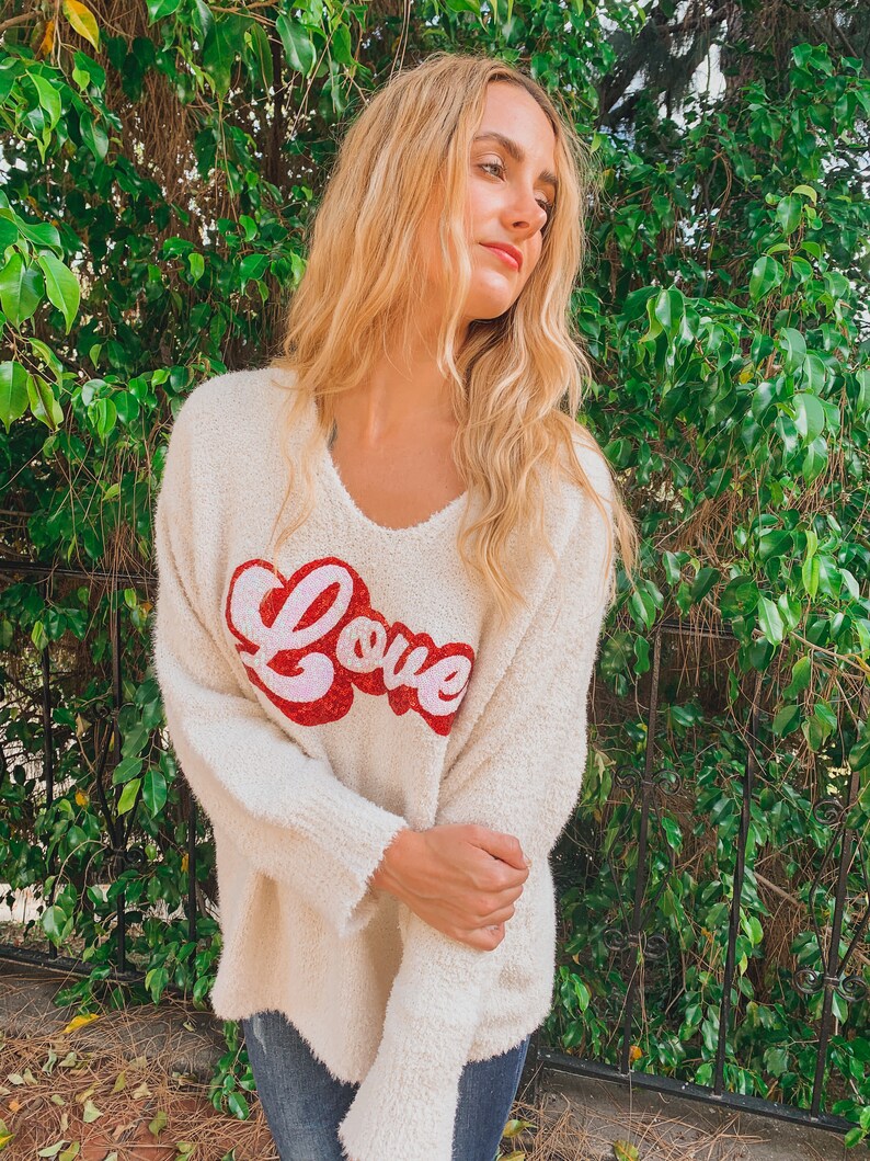 May include: A white fuzzy sweater with a red and pink "Love" graphic on the front.