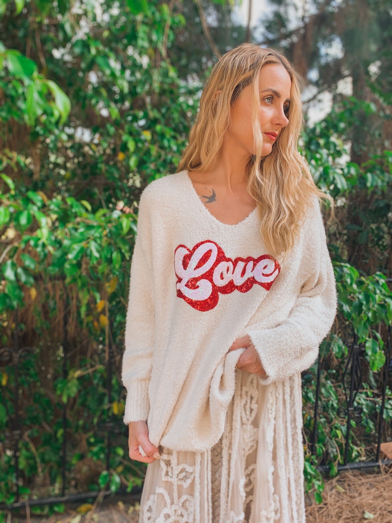May include: A white fuzzy sweater with a red and white "Love" graphic on the front. The sweater is worn over a white lace skirt.