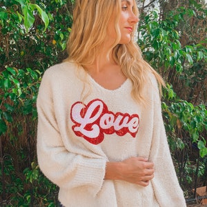 May include: A white fuzzy sweater with a red and pink "Love" graphic on the front.