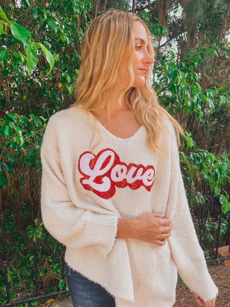 May include: A white fuzzy sweater with a red and pink "Love" graphic on the front.