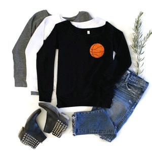 May include: Black sweatshirt with a basketball graphic on the front. The sweatshirt is paired with blue jeans and black studded boots.