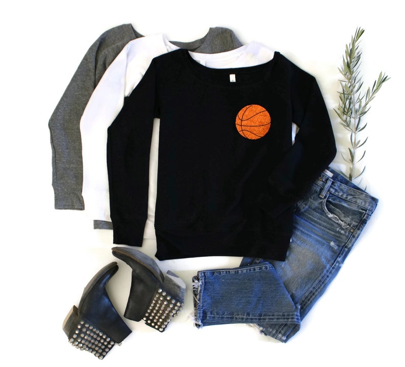 May include: Black sweatshirt with a basketball graphic on the front. The sweatshirt is paired with blue jeans and black studded boots.