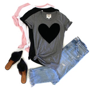 May include: A gray t-shirt with a large black heart on the front. The shirt is paired with light blue jeans and black fuzzy slippers.