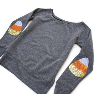 May include: Grey sweatshirt with a candy corn design on each elbow. The candy corn is made of sequins in orange, yellow and white.