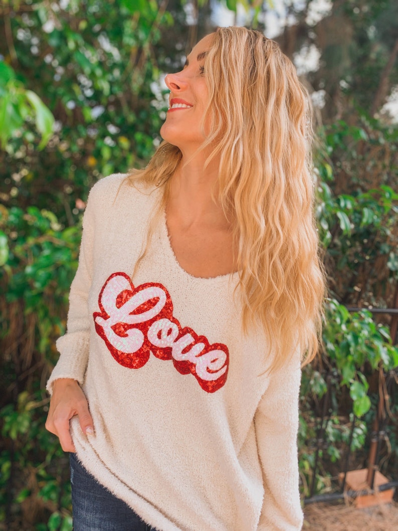 May include: A white fuzzy sweater with a red sequined "Love" graphic.
