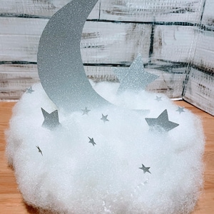 May include: A silver glitter moon and stars on a white fluffy cloud. The moon is a crescent shape and the stars are five-pointed.