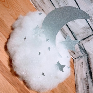 Pode incluir: Uma nuvem branca e fofa com uma lua crescente prateada com glitter e estrelas prateadas com glitter.