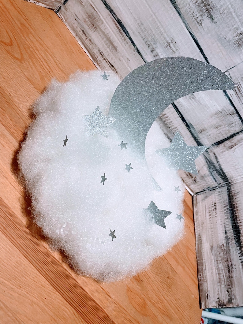 Pode incluir: Uma nuvem branca e fofa com uma lua crescente prateada com glitter e estrelas prateadas com glitter.