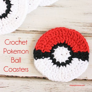 May include: Four crocheted Pokemon ball coasters in red, white and black. The coasters are on a white wooden surface. Crochet Pokemon Ball Coasters.