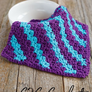 May include: A handmade, square crochet dishcloth in a purple and turquoise chevron pattern. The dishcloth is resting on a wooden surface next to a white bowl. Text on the image reads "Mini C2C Crochet Dishcloth Pattern".
