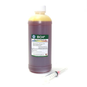 Op de afbeelding: Een fles BCH Standard Bulk Ink met een witte dop en een etiket. De inkt heeft een donkerroodbruine kleur. Een spuit staat naast de fles. Het etiket bevat productinformatie en het BCH-logo.
