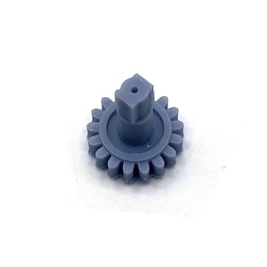 May include: A small, gray gear with a central square post and a circular base. The gear has multiple teeth around its perimeter and a hole in the top of the post. The object is set against a white background.