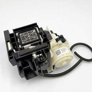 May include: A black and cream-colored printer ink pump assembly featuring a rectangular grid-patterned filter, a cylindrical motor housing with a white label containing QR codes and the text 1862911 2NA435L 0311, and a black rubber tube.