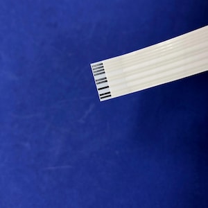 May include: A white flat ribbon cable with black lines running along the length of the cable.