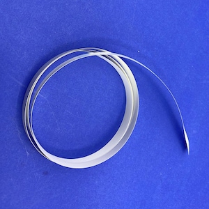 May include: A coiled, thin, white strip of material against a blue background. The strip appears to be made of a flexible, possibly paper-like substance, and is curled into a circular shape. The end of the strip extends outward.