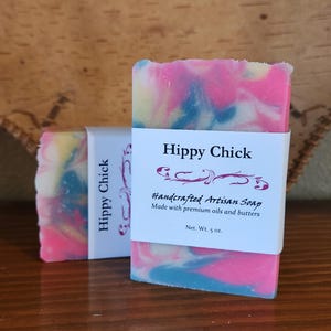 May include: Two bars of artisan soap with a colorful swirl design in pink, blue, and yellow. The soap is labeled "Hippy Chick" and "Handcrafted Artisan Soap." Each bar weighs 5 oz.