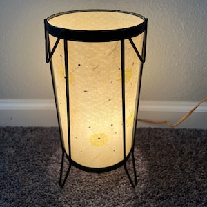 May include: A black metal floor lamp with a white paper shade. The shade has a geometric pattern of yellow and blue stars.