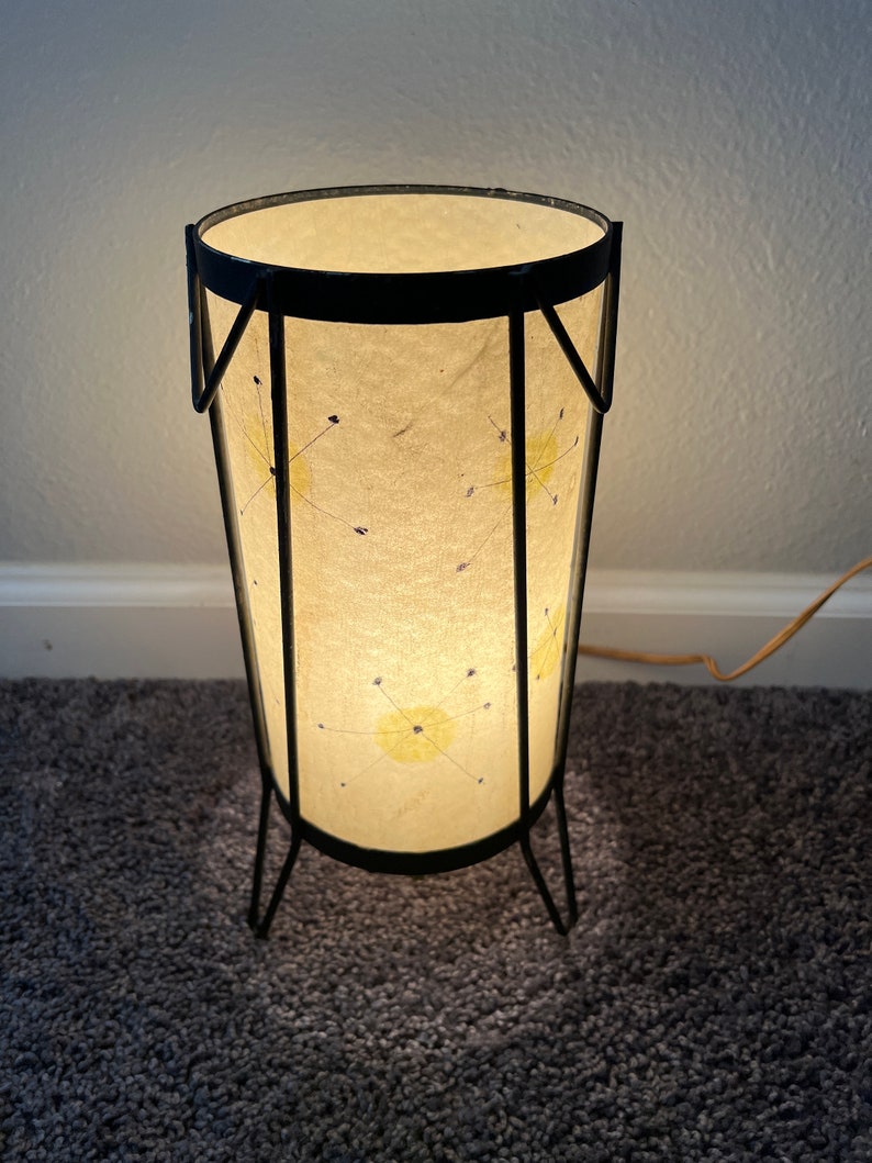 May include: A black metal floor lamp with a white paper shade. The shade has a geometric pattern of yellow and blue stars.