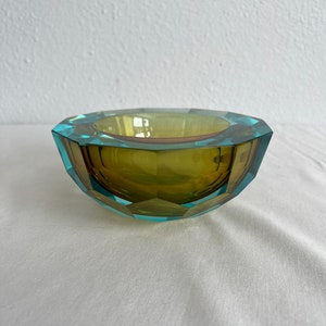 Op de afbeelding: Een gefacetteerde glazen kom met een groen en blauw kleurenschema. De kom heeft een geometrische vorm en is gemaakt van helder glas.