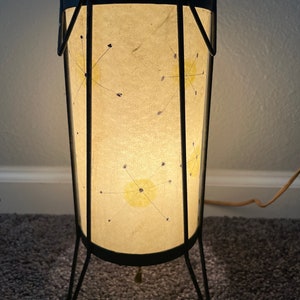 May include: A black metal floor lamp with a white paper shade. The shade has a starburst design with yellow and blue accents.