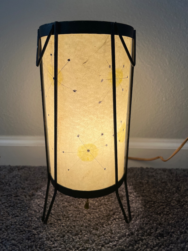 May include: A black metal floor lamp with a white paper shade. The shade has a starburst design with yellow and blue accents.