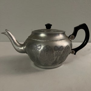 May include: A silver teapot with a black handle and a floral design. The teapot has a black knob on the lid.