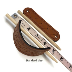 May include: Two wooden hair sticks, one with a brown leather wrap and the other with a brown leather wrap with a woven pattern, are measured with a tape measure. The tape measure reads 2, 3, 4, 5, 6, and 7 inches.  Standard size.