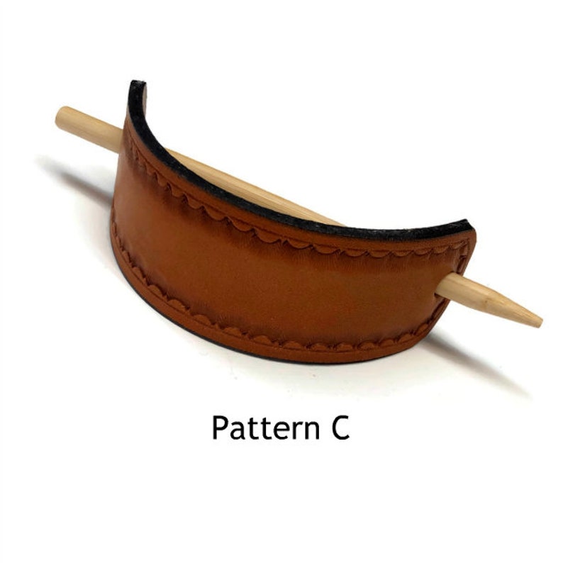 May include: A brown leather hair stick with a decorative stitch pattern. The stick is made of wood and has a rounded end. The text "Pattern C" is printed below the hair stick.