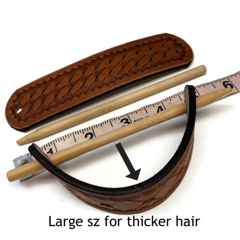 May include: A brown leather hair stick with a woven design. The stick is 4 inches long and is shown with a measuring tape. The text "Large sz for thicker hair" is visible below the stick.