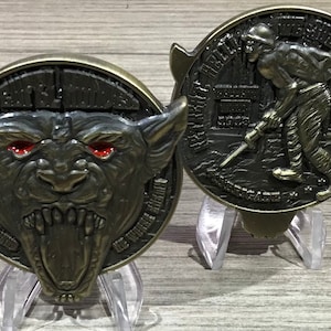 May include: Two bronze challenge coins. One coin features a snarling wolf with red eyes and the text "The Devil's Own". The other coin features a soldier with a jackhammer and the text "We Built the Roads for This".