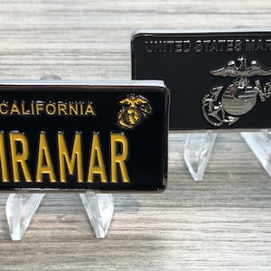 May include: Two black metal license plate style keychains with gold lettering and emblems. The top keychain says "United States Marine Corps" with the Marine Corps emblem. The bottom keychain says "California MIRAMAR" with the Marine Corps emblem.