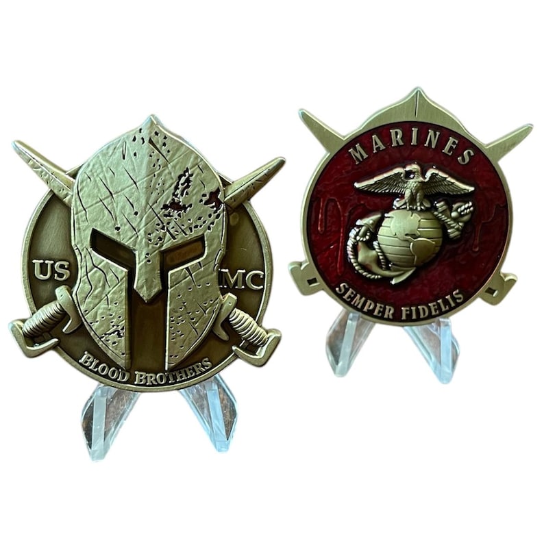 K&ouml;nnte beinhalten: Zwei antike, goldfarbene USMC-Challenge-M&uuml;nzen. Eine M&uuml;nze zeigt einen spartanischen Helm und gekreuzte Schwerter mit dem Text "US MC" und "Blood Brothers". Die andere M&uuml;nze hat einen roten Hintergrund mit dem Text "Marines" und "Semper Fidelis".