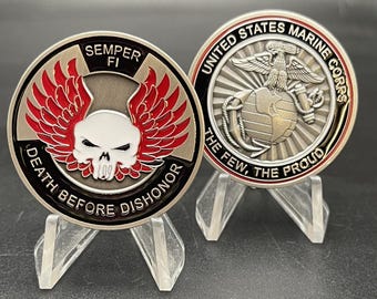 Puede incluir: Dos monedas redondas de metal sobre soportes transparentes. Una moneda presenta una calavera con alas rojas y el texto "DEATH BEFORE DISHONOR" y "SEMPER FI". La otra moneda tiene las palabras "UNITED STATES MARINE CORPS" y "THE FEW, THE PROUD".