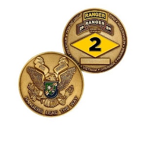 May include: Two gold-colored military challenge coins. One coin features a bald eagle with the text "Rangers Lead The Way". The other coin features a yellow diamond with the number "2" and the text "2nd Ranger Bn. October 1974 Ft. Benning, GA. Point Du Hoc Myitkyina Korea Vietnam Grenada Panama Afghanistan Iraq".