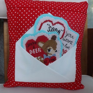 Peut inclure: Un oreiller rouge à pois blancs présente une enveloppe blanche avec un rabat plié. À l'intérieur de l'enveloppe se trouvent trois cartes brodées avec des cœurs et des messages qui disent "You're a Deer", "So Sweet", et "You Want to Be Mine".