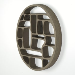 Op de afbeelding: Een ronde wandplank gemaakt van bruin keramiek met een geometrisch patroon van open vakken. De plank is ontworpen om aan de muur te worden gemonteerd.