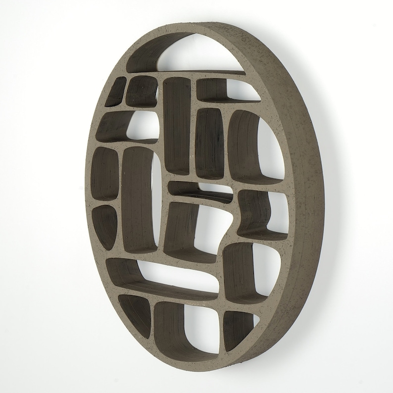 Op de afbeelding: Een ronde wandplank gemaakt van bruin keramiek met een geometrisch patroon van open vakken. De plank is ontworpen om aan de muur te worden gemonteerd.