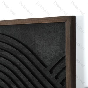 May include: A black and brown framed wall art piece with a carved design of curved lines. The design is reminiscent of a wave or a mountain range.