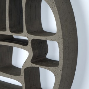 Op de afbeelding: Een donkergrijze keramische wandplank met een unieke, organische vorm en meerdere open vakken. De plank is ontworpen om aan de muur te worden gemonteerd en biedt een decoratieve en functionele opbergoplossing.