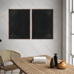 May include: Two black framed wall art pieces with a geometric design of concentric circles and lines. The art is hanging on a white wall above a wooden table with a vase and books.