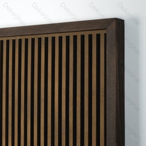 Op de afbeelding: Een bruin houten frame met verticale latten, die een decoratief wandpaneel vormen. De latten zijn gerangschikt in een herhalend patroon van licht- en donkerbruin.