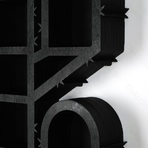 May include: Close-up of a black, geometric wooden structure with a grid-like pattern and a curved element. The design features sharp, angular edges and a textured surface. The background is white.