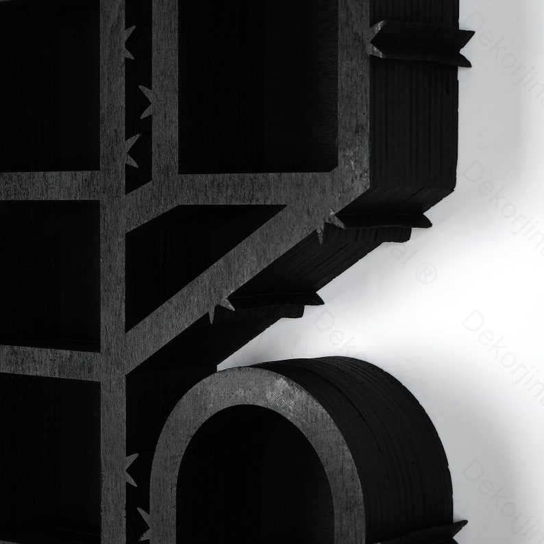May include: Close-up of a black, geometric wooden structure with a grid-like pattern and a curved element. The design features sharp, angular edges and a textured surface. The background is white.