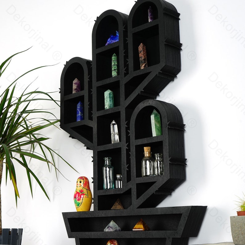 May include: A black wooden cactus-shaped wall shelf filled with various crystals, glass bottles, and a Matryoshka doll. The shelf has multiple compartments and a textured surface, creating a unique display for home decor.