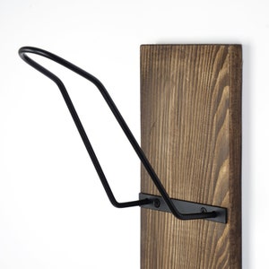 May include: A black metal hat rack mounted on a brown wooden board. The rack is shaped like a curved hook.