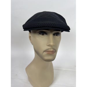 May include: A black newsboy cap with a textured knit design on the front and a solid top. The cap is displayed on a mannequin head against a white background. The cap has a short, stiff brim.