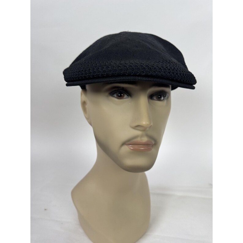 May include: A black newsboy cap with a textured knit design on the front and a solid top. The cap is displayed on a mannequin head against a white background. The cap has a short, stiff brim.