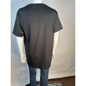 May include: A black short-sleeved t-shirt on a mannequin, paired with blue jeans. The t-shirt is plain and appears to be made of a soft fabric. The mannequin is positioned against a white backdrop.