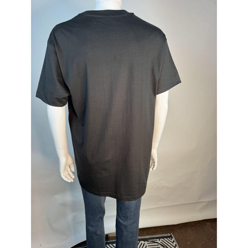May include: A black short-sleeved t-shirt on a mannequin, paired with blue jeans. The t-shirt is plain and appears to be made of a soft fabric. The mannequin is positioned against a white backdrop.